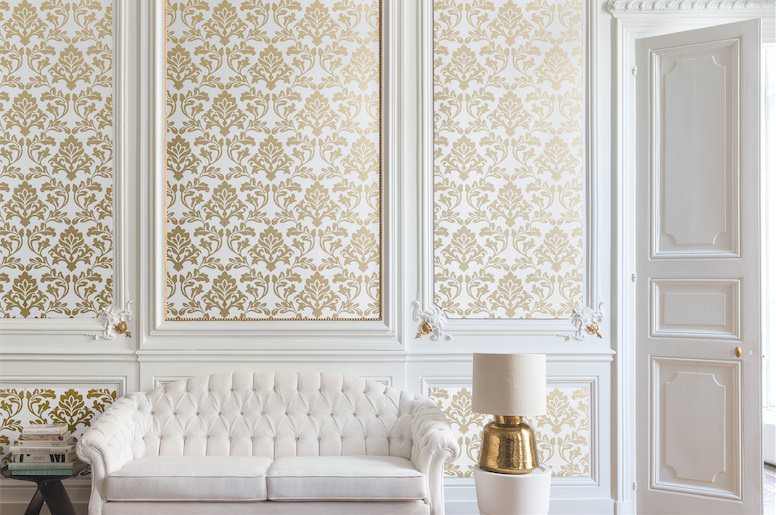 اتاق پذیرایی کلاسیک با دیوار و مبل های سفید که سطح داخلی دیوارهای قاب بندی شده آن کاغذ دیواری شده است
